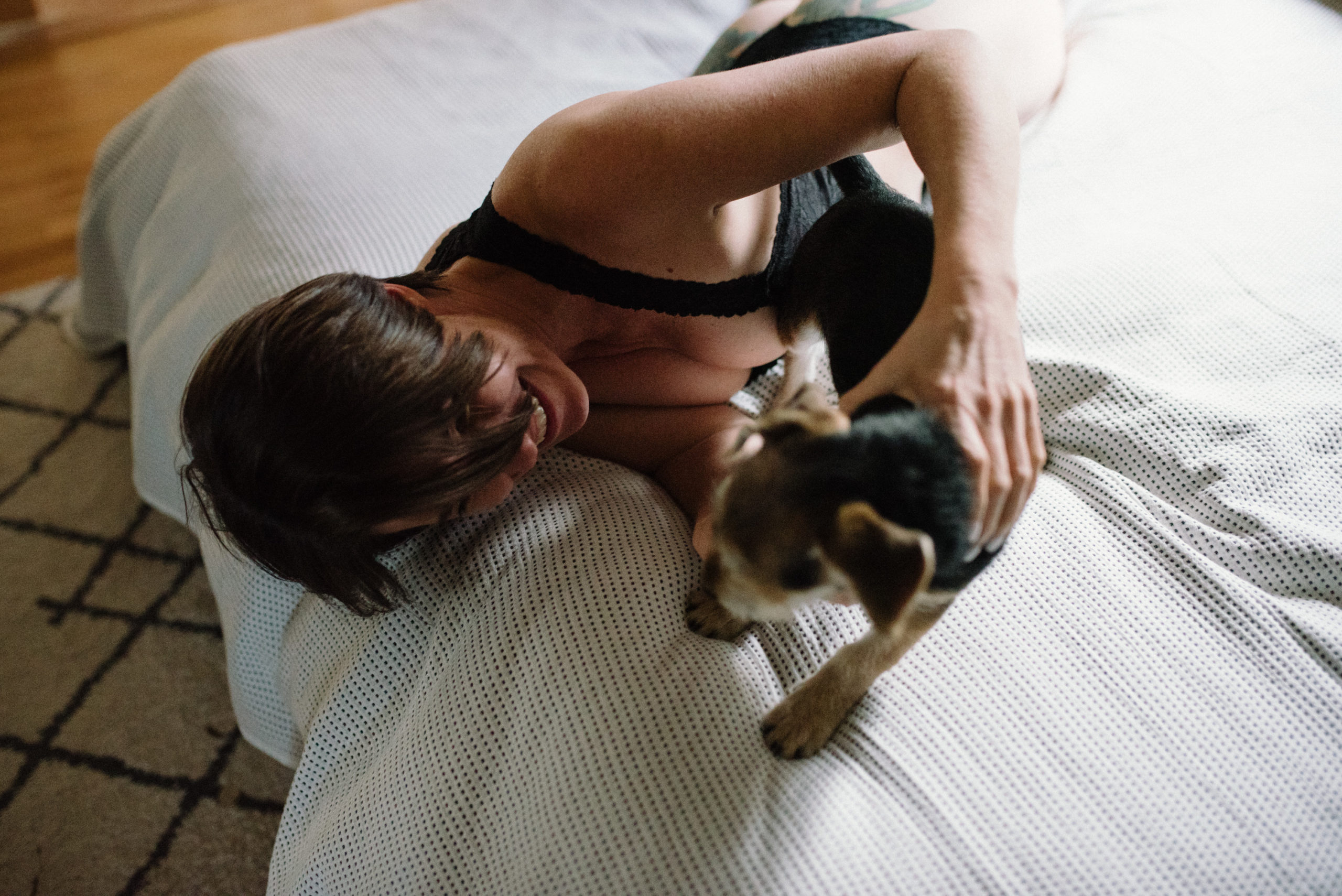 lady in underwear on bed playing with dog