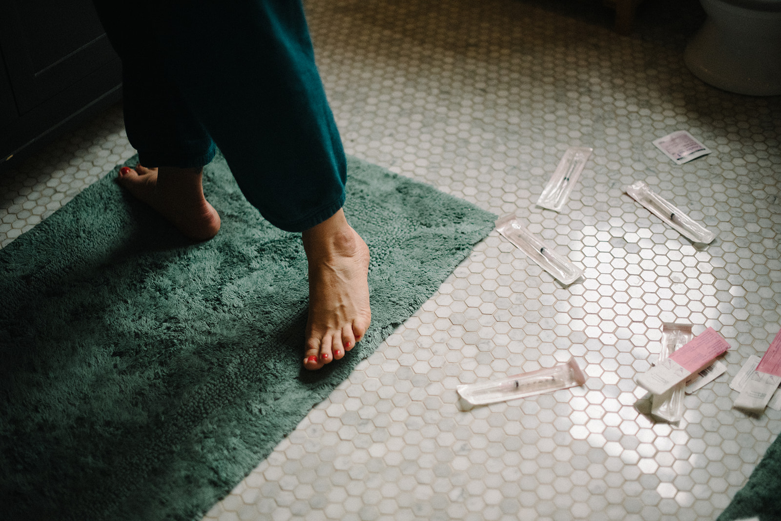 feet of a pregnant woman standing in the bathroom with IVF needles scattered on the ground