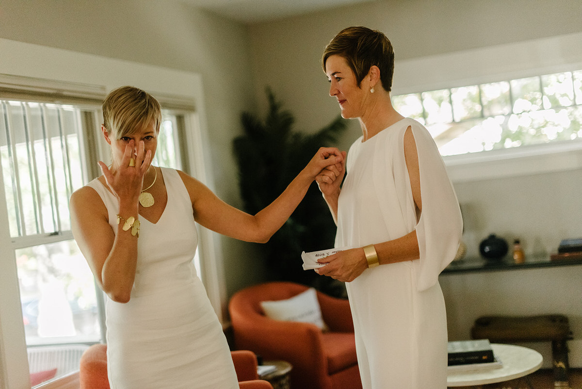two brides seeing each other for the first time on their wedding day. one is crying while the other is holding her hand.