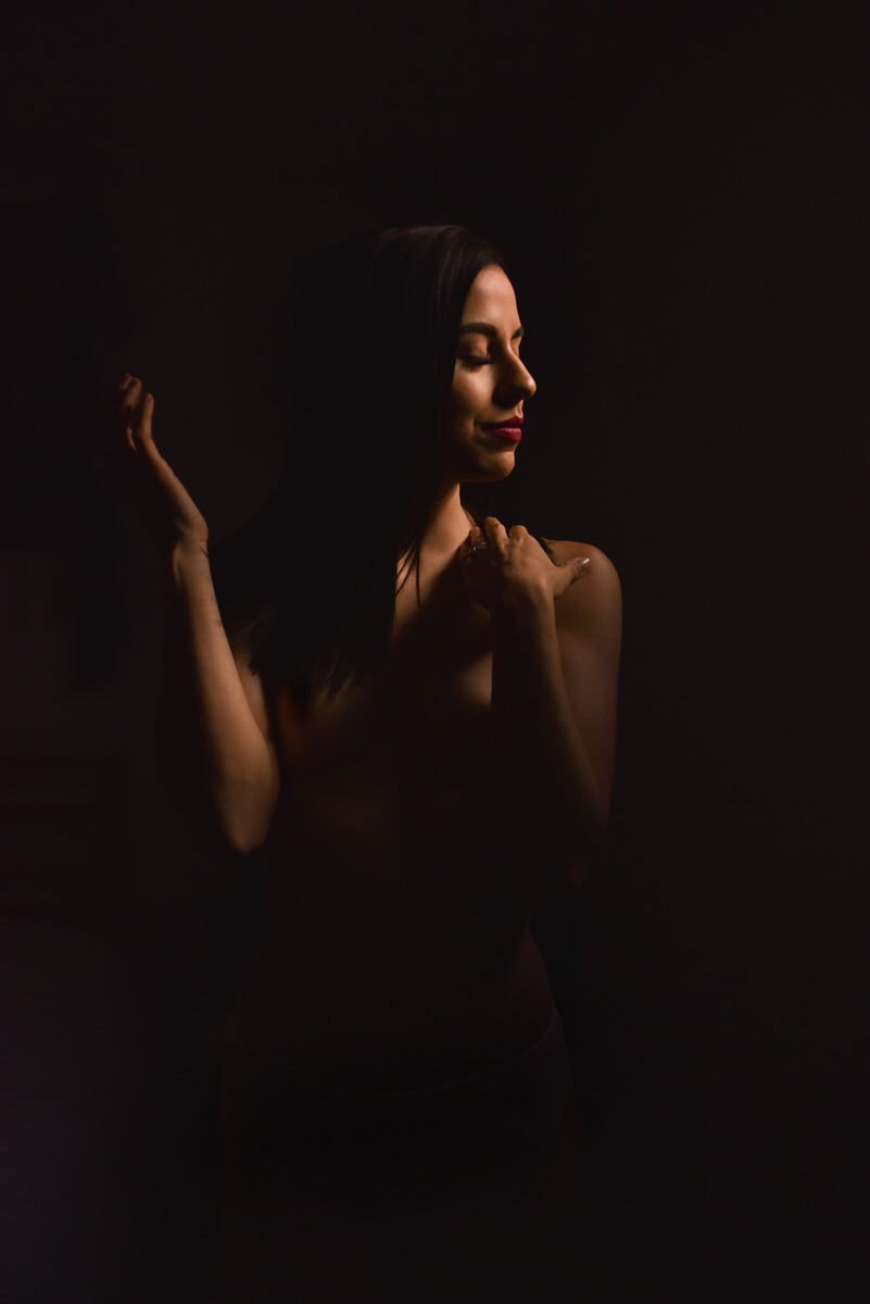 semi nude portrait of a woman with light only illuminating her shoulder and face.