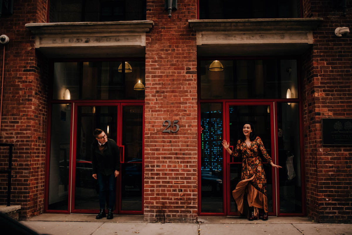 a female couple standing in two separate doorways of an old brick building in Dumbo Brooklynone is wearing a dress blowing in the wind.